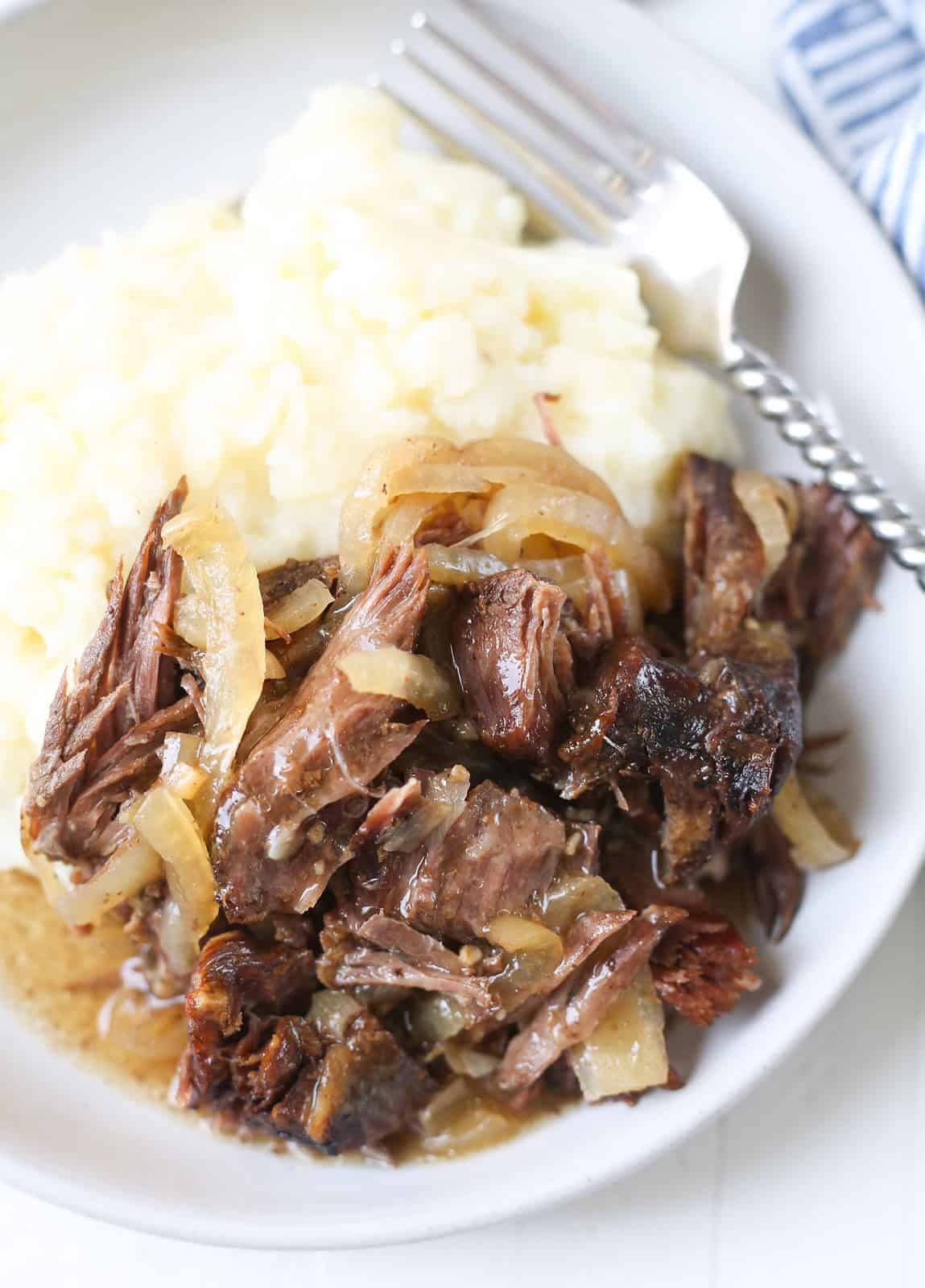 Slow cooker French onion pot roast served with mashed potatoes and caramelized onions.