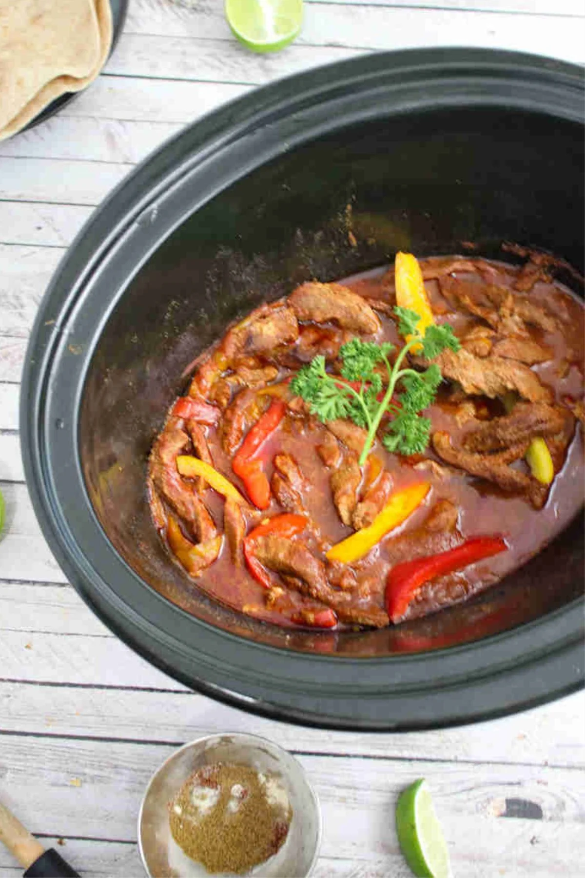Slow cooker beef fajitas with sliced peppers and savory sauce cooking inside a crockpot.