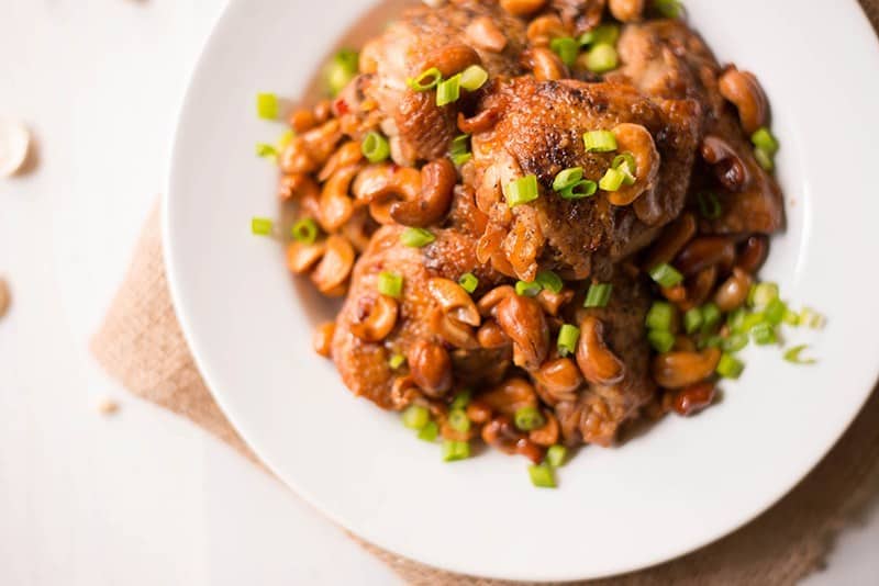 Slow cooker cashew chicken on a white plate topped with green onions.