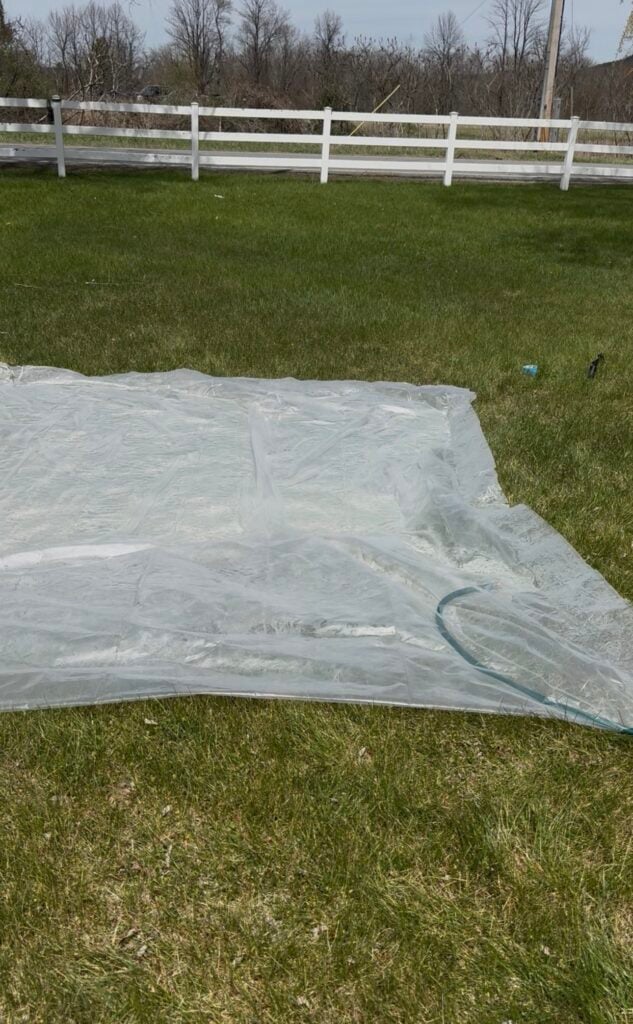 Large homemade water blob made from plastic sheeting filling with water from a garden hose in a grassy backyard.