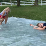 Two young girls playing and bouncing on a giant homemade water blob in the backyard.