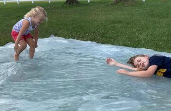 Two young girls playing and bouncing on a giant homemade water blob in the backyard.