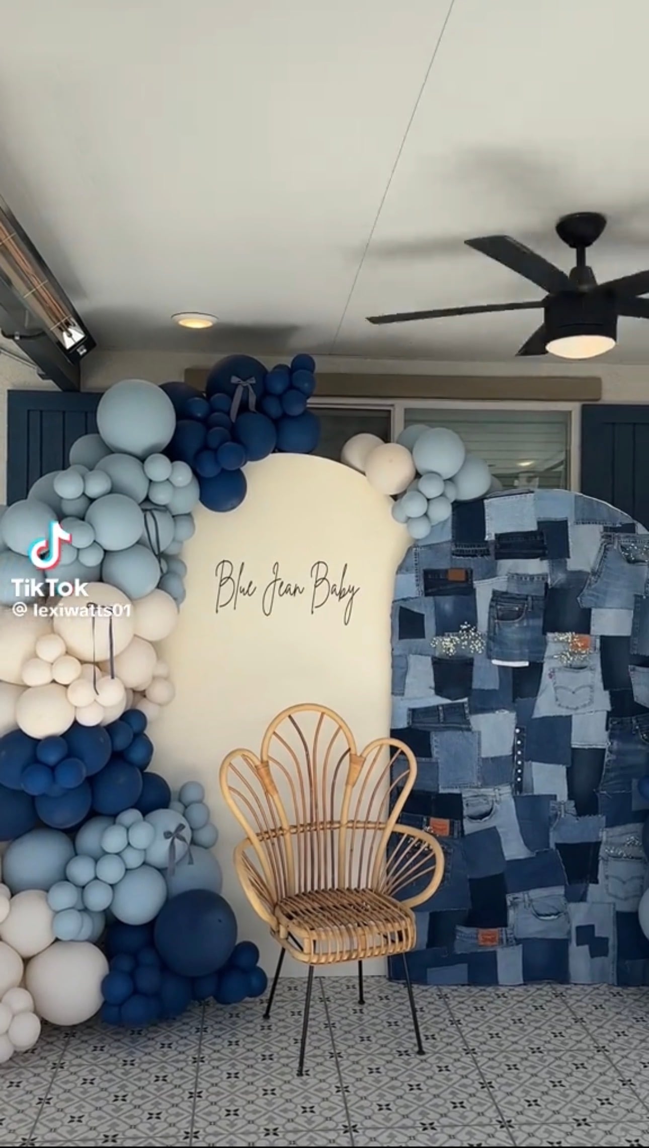 Blue jean baby shower backdrop with patchwork denim, blue and white balloon garlands, and a rattan chair for a blue jean baby shower theme.