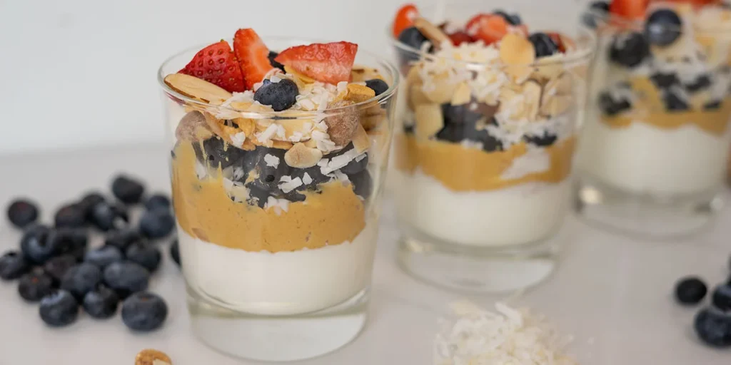 Easy gestational diabetes breakfast consisting of a Greek yogurt parfait layered with peanut butter, blueberries, strawberries, coconut, and sliced almonds.
