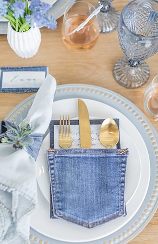 Blue jean pocket holding gold silverware on a blue and white baby shower place setting with lavender accents for a blue jean baby shower theme.