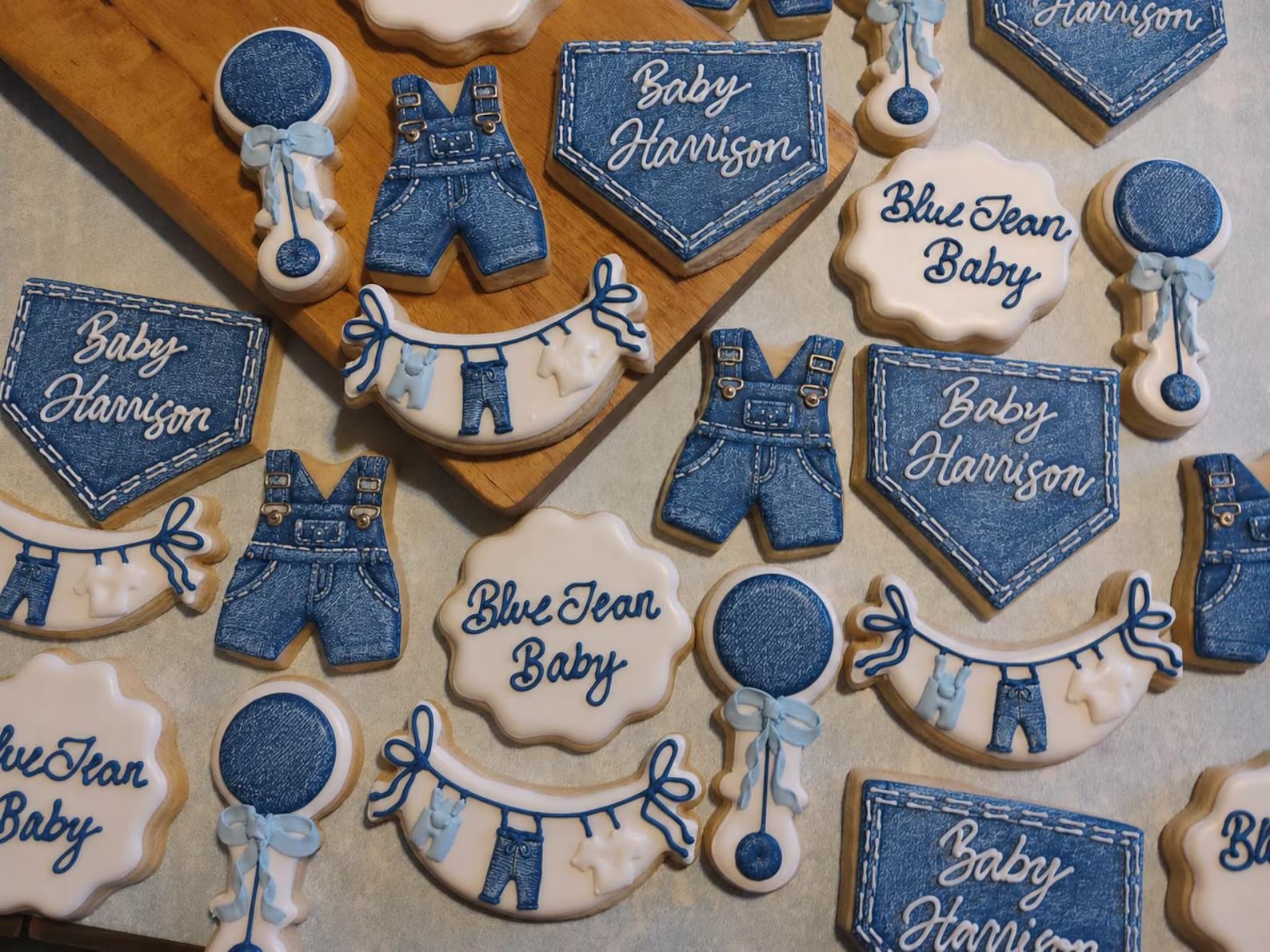 Blue Jean Baby shower cookies decorated with denim overalls, jean pockets, baby clotheslines, rattles, and blue and white icing.