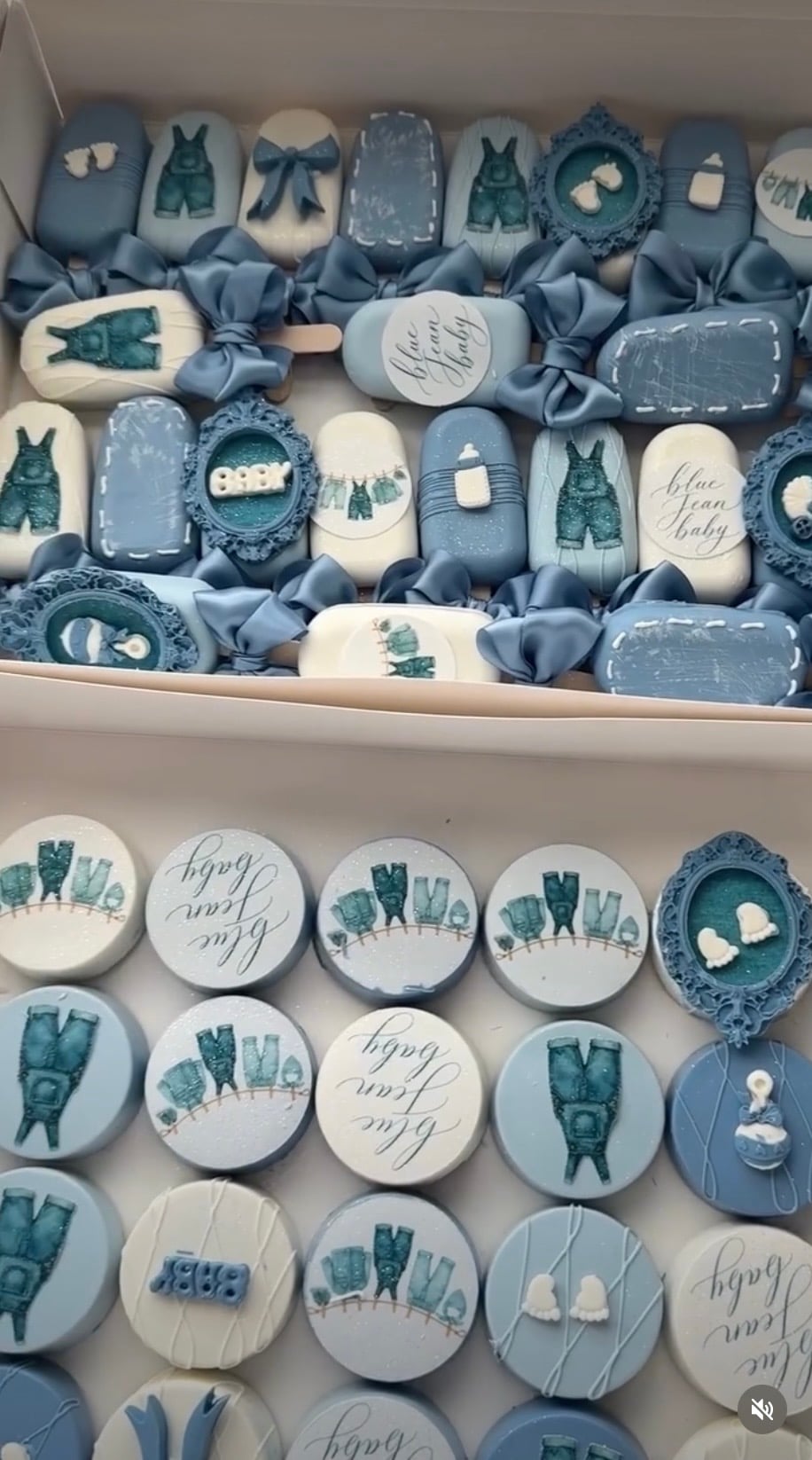 Blue and white Blue Jean Baby cakesicles decorated with denim overalls, jean pockets, baby bottles, bows, and tiny baby clothes.