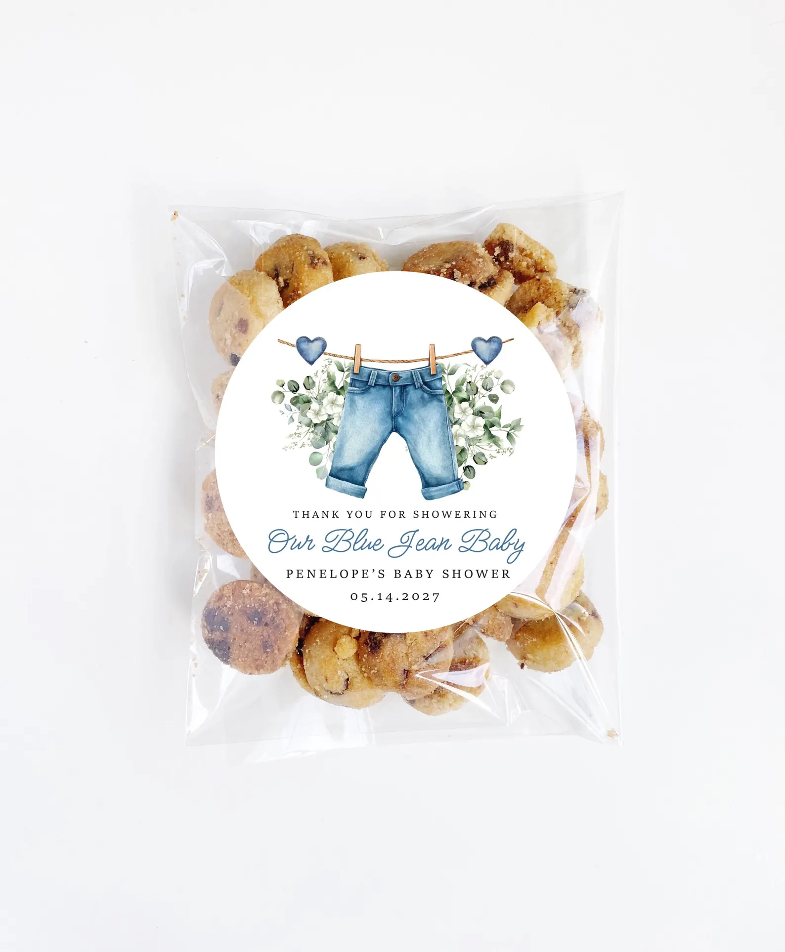 Clear bag of mini cookies with a personalized sticker featuring blue jeans, greenery, and blue hearts for a blue jean baby shower theme.