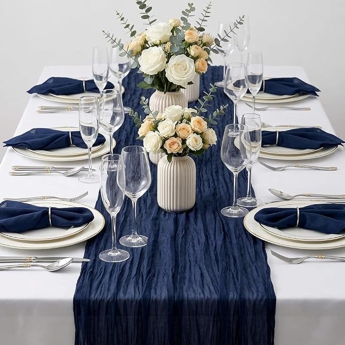 White baby shower table with a dark blue table runner, navy napkins, white place settings, and white floral centerpieces for a blue jean baby shower theme.