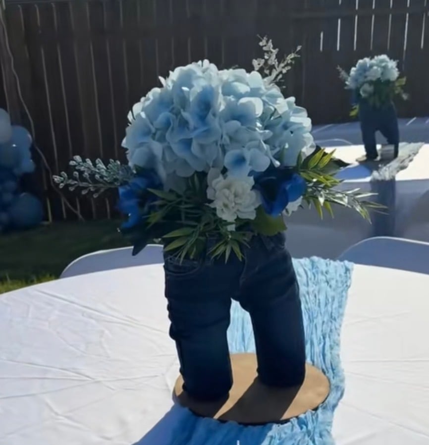 Tiny blue jeans filled with blue and white flowers and greenery used as a table centerpiece for a blue jean baby shower theme.