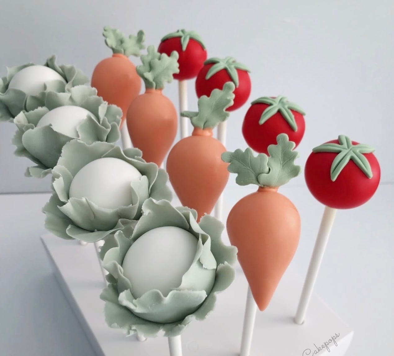 Locally grown baby shower cake pops decorated as carrots, tomatoes, and leafy green cabbages in soft garden-inspired colors.