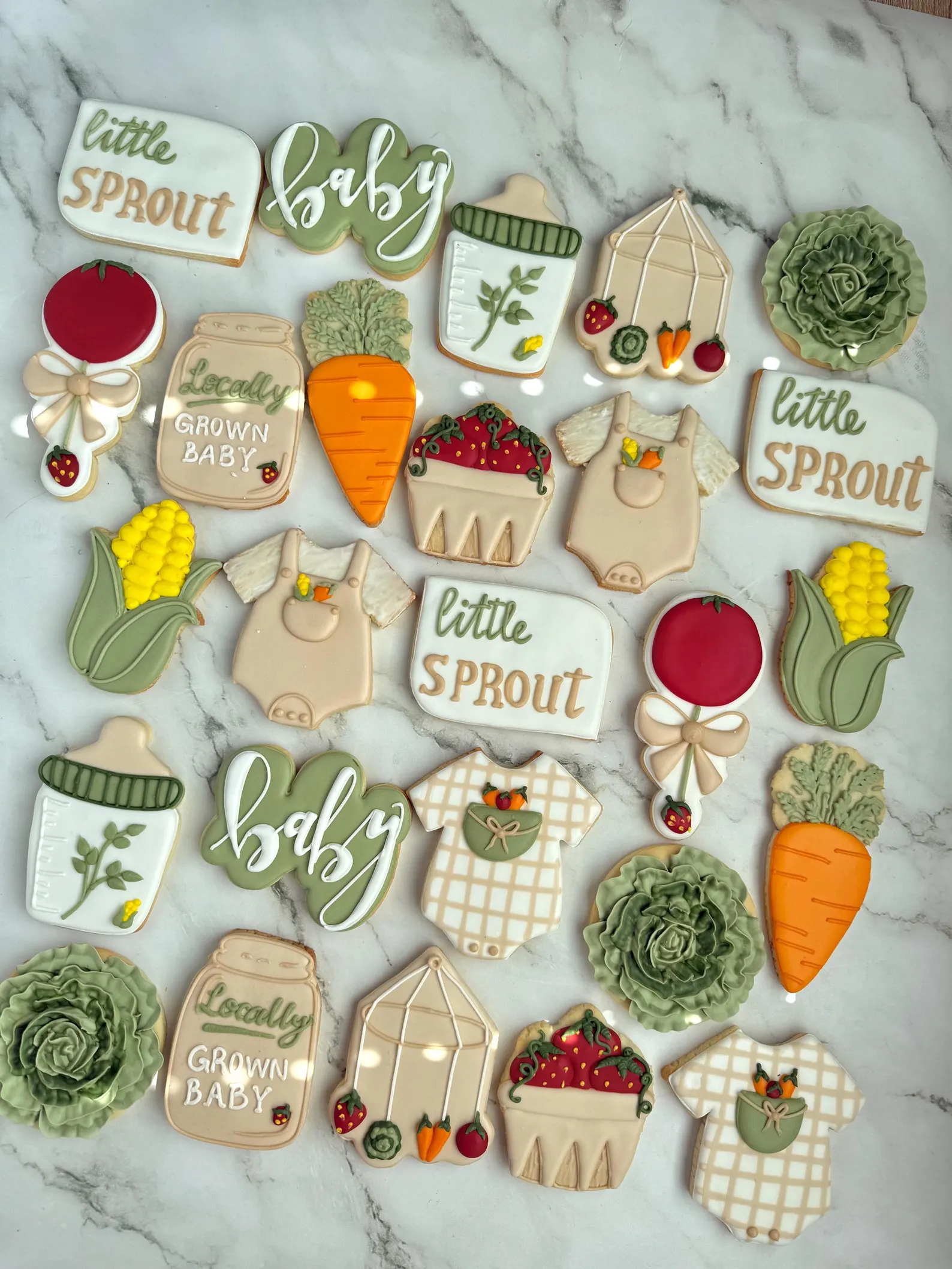 Locally grown baby shower cookies decorated with carrots, tomatoes, corn, lettuce, strawberries, baby onesies, greenhouses, and “little sprout” garden details.