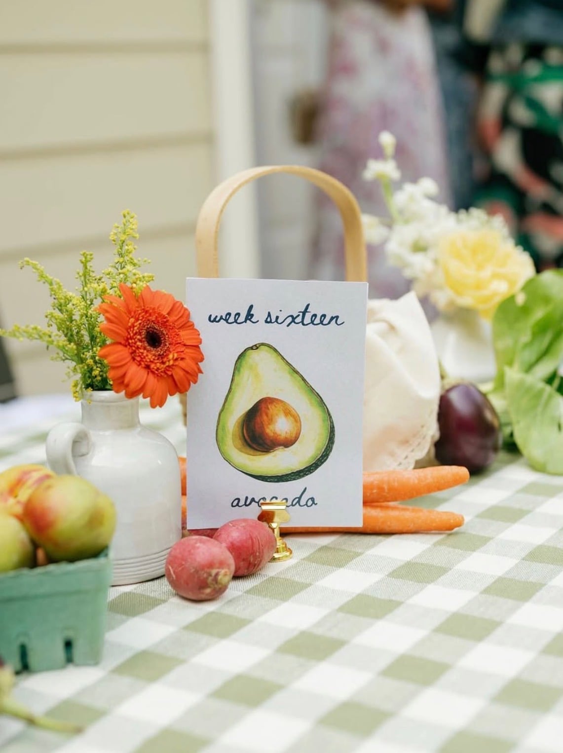 Locally grown baby shower table number featuring week sixteen with an avocado, part of a pregnancy week table number set showing the fruit or vegetable baby is the size of each week.