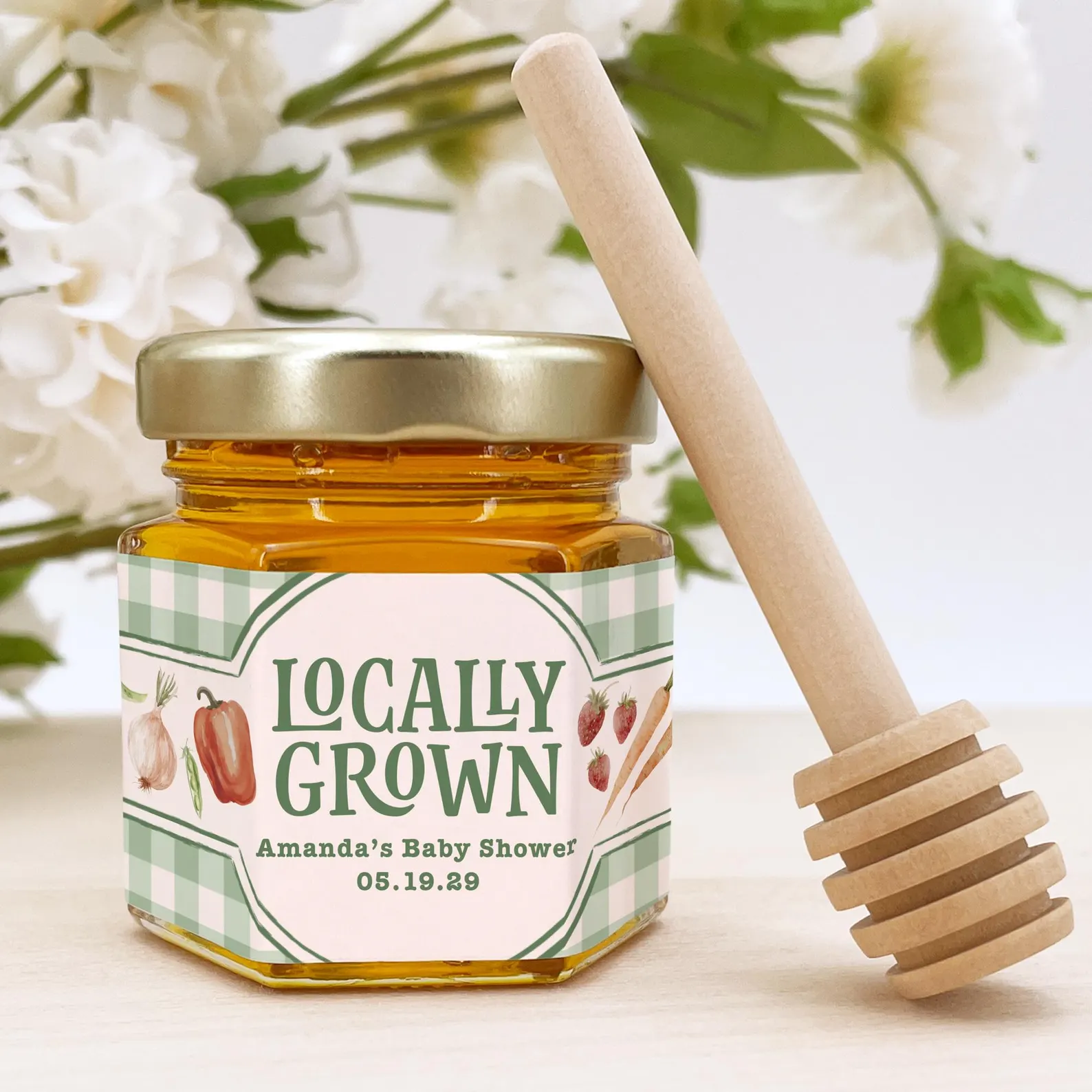 Locally grown baby shower favor featuring a personalized jar of honey with a sage green gingham vegetable label and wooden honey dipper.
