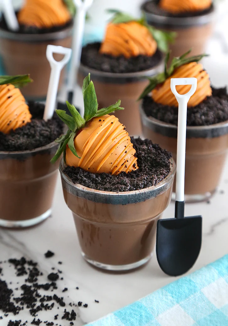Locally grown baby shower dessert cups made with chocolate pudding and crushed cookie “dirt,” topped with carrot-shaped chocolate-covered strawberries and mini shovel spoons.